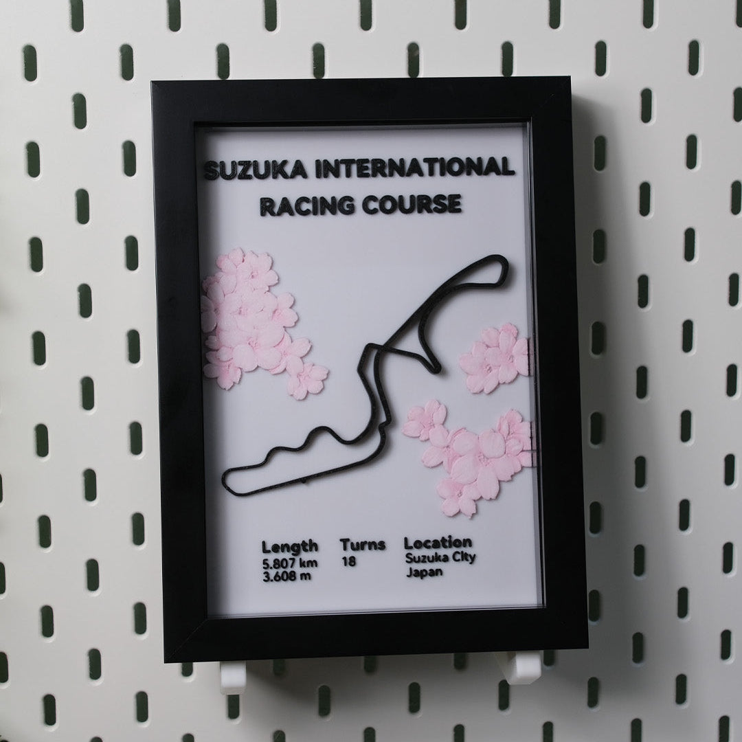 Framed map of Suzuka International Racing Course with cherry blossom decorations on a pegboard wall.