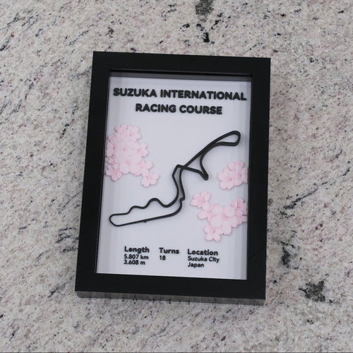 Framed map of Suzuka International Racing Course with cherry blossom decorations on a textured surface.
