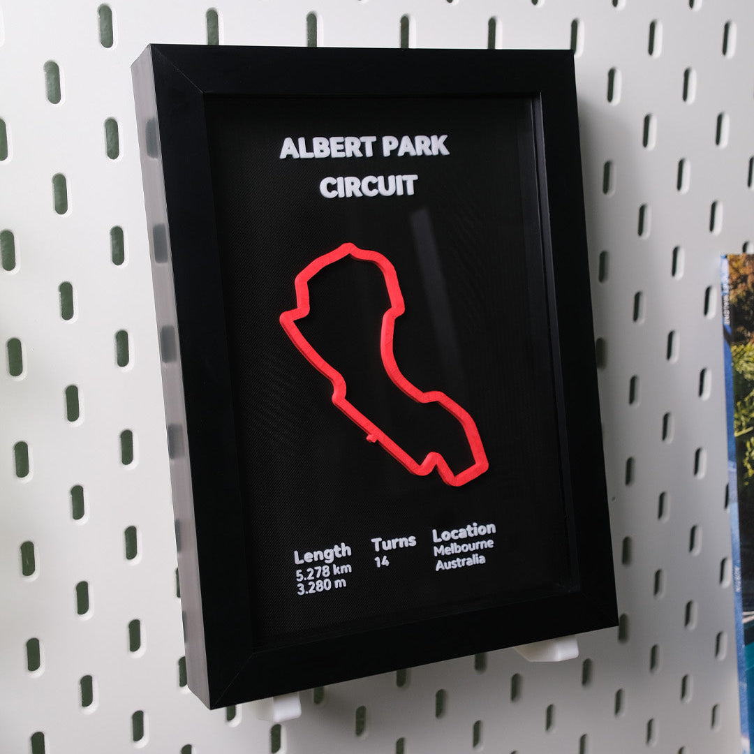 Framed poster of Albert Park Circuit with red track outline on a black background, mounted on a pegboard.